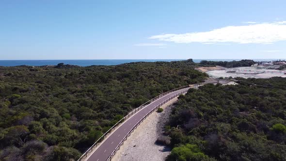 Aerial Flyover Coastal Cyclepath Winding Through Sand Dunes With Ocean alt