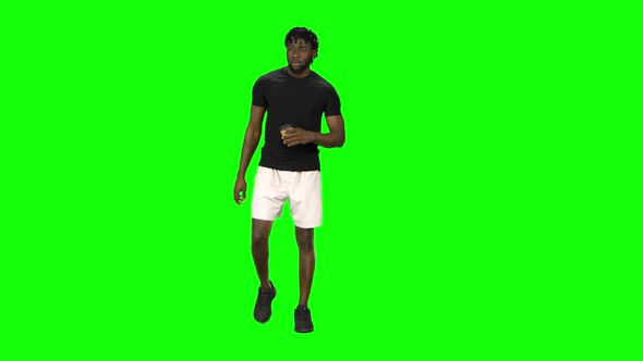 African American Man Is Walking and Drinking Coffee at Green Screen, Chroma Key. Front View. alt