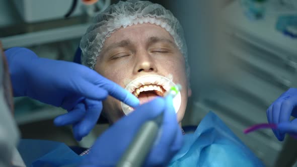 Closeup Man in Dental Chair with Doctor and Nurse Using Drill and Sucking Tube in Slow Motion alt