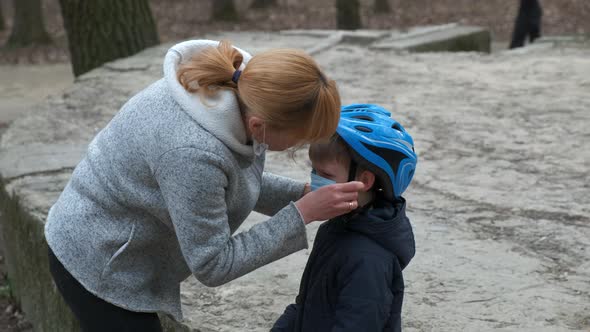 Mother puts on a medical mask for her son before Cycling in the Park.