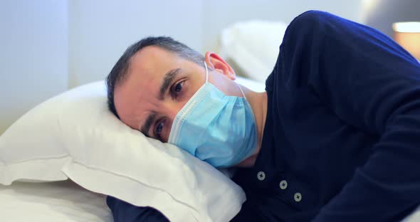 Young Man with Protective Mask and Covid 19 Symptoms in Bed