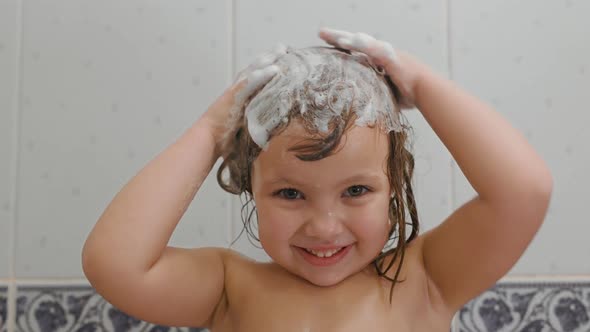 Cute Little Girl Shampoos Her Hair and Smiles in the Bath at Home