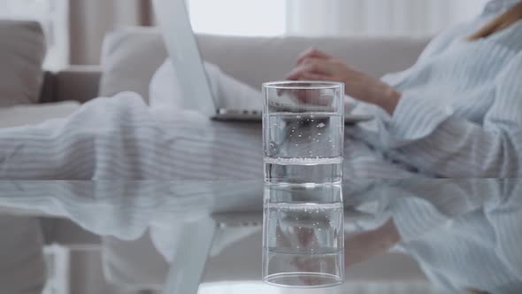 Glass of Iced Water on Table on the Background of a Woman with a Computer alt