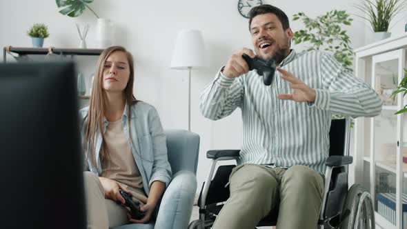 Disabled Man Playing Videogame with Girlfriend Winning Dancing in Wheelchair at Home alt