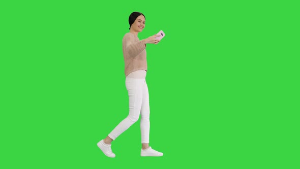 Pretty Smiling Female in Casual Clothes Taking Selfie While Walking on a Green Screen, Chroma Key. alt