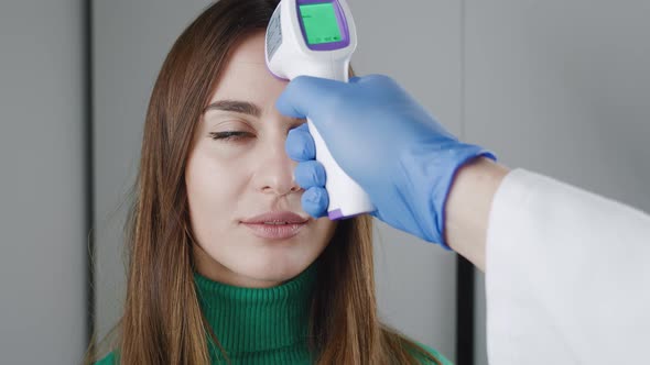 Temperature Measurement By Electronic Infrared Thermometer for a Young Woman in Green Sweater alt