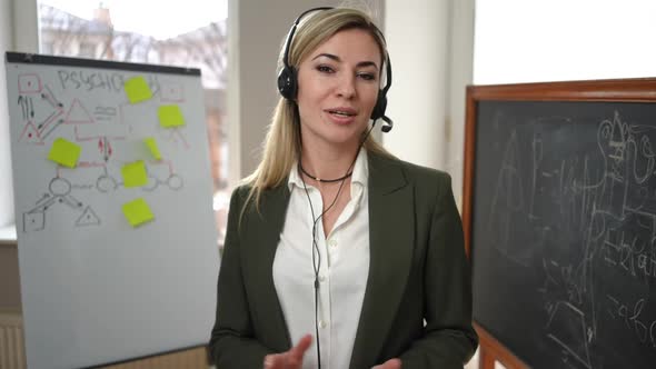 Portrait of Confident Woman in Headphones Talking Looking at Camera Standing in Classroom with alt
