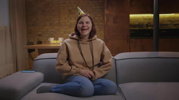 Young Cheerful 30s Woman Wearing Birthday Hat Congratulating with Birthday Talking at Camera Sitting alt