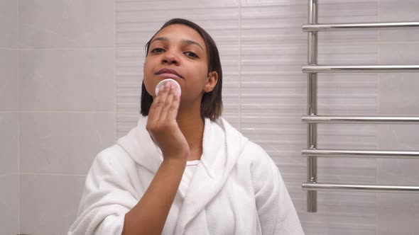 A Woman with Dark Skin Washes Her Face with Foam and Water in the Bathroom