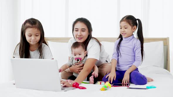Busy single mom concept, mother working on laptop and caring for her baby and little daughte