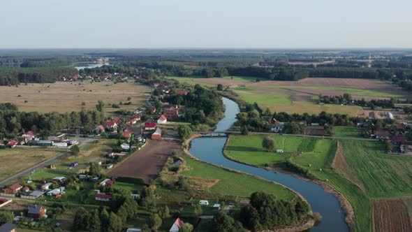 Aerial rural shot of a curvy river with a wooden bridge, running by a small farming village. Lake vi alt
