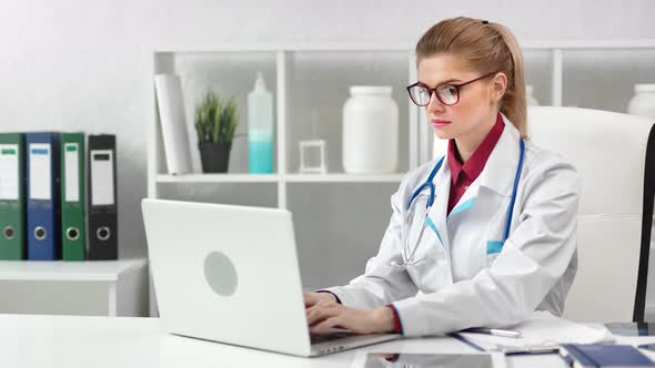 Focused Young Beautiful Female Doctor Working Using Laptop Pc at Modern Clinic alt