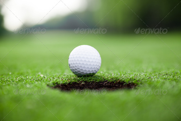 Golf ball on green meadow.  golf ball on lip of cup - Stock Photo - Images