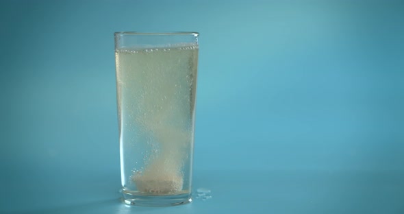 A Vitamin C Tablet Is Thrown Into a Transparent Glass Glass with Water. The Effervescent Pink Tablet