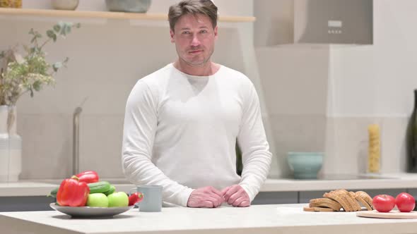Middle Aged Man Looking at the Camera While Standing in Kitchen alt