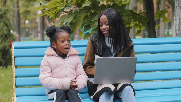 Young African American Mom with Daughter on Bench in City Park Friendly Family Together Looking in alt
