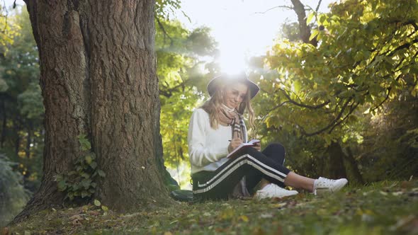 Smiling Woman Sitting Near the Tree in the Park alt