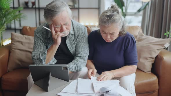old retired asian senior couple checking and calculate financial billing together on sofa alt