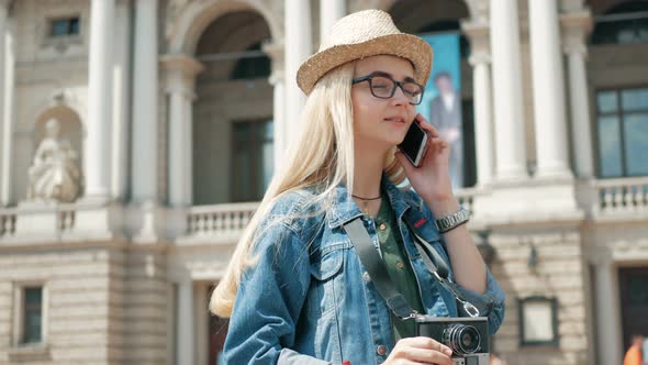 Young cute tourist is talking on the phone outside, wearing hat, glasses