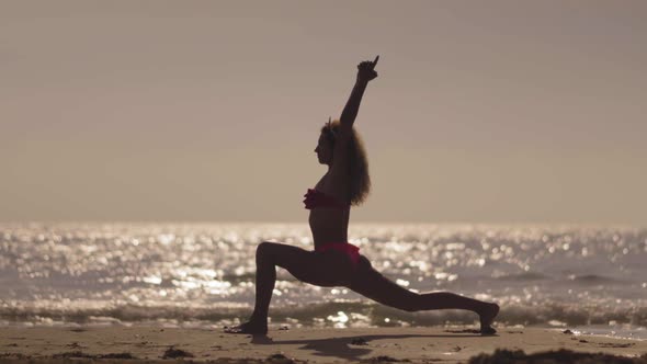 The Girl Practic Yoga on the Beach at Sunset. Young Girl Doing Exercise at a Tropical Beach alt