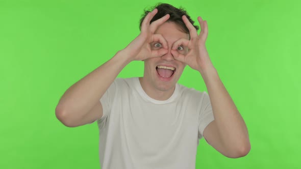 Funny Young Man with Binocular Gesture Searching on Green Background alt