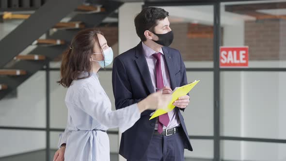 Young Rich Caucasian Woman in Covid Face Mask Explaining Flat Renovation to Man Writing Plan alt