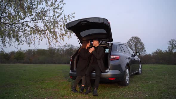Happy Loving Couple of Travelers Stand Next to Car and Admire Beautiful Sunset alt