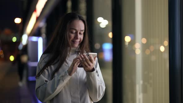 Charming Female Dweller of Megapolis is Using Smartphone Outdoors in Night Sending Message alt