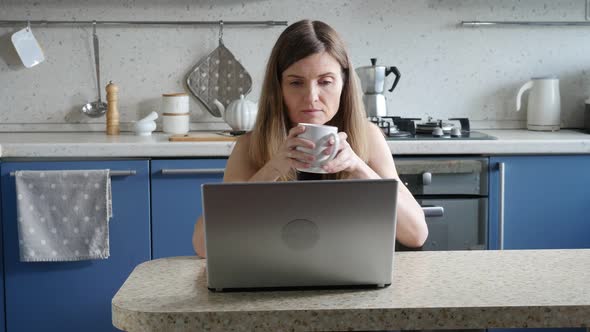 Business Woman Having Coffee and Telecommuting with Laptop in the Kitchen