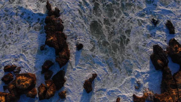 Spectacular top down aerial drone view of rough waves crashing the rock shore alt