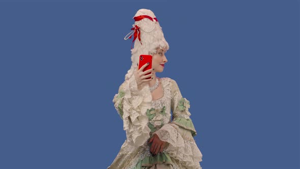 Portrait of Courtier Lady in White Vintage Lace Dress and Wig Talking for Video Chat Using Mobile alt