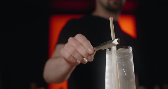 Barkeeper Inserts the Straw to the Cocktail with Ice Cubes and Soda Water in Slow Motion Limonade on alt