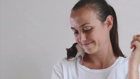 Young Woman Feeds a Pet Rat Which Sits on Her Shoulder with Cornflake