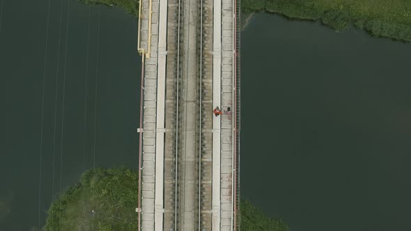 Aerial View of Two People Walking on a Bridge Over a River alt