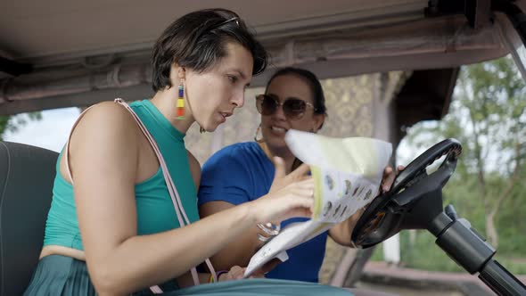 Two Excited Tourists Female Friends Sitting In A Golf Cart Searching Direction On A Tour Map In alt
