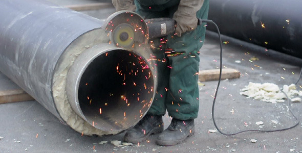 Worker cutting pipe with grinder