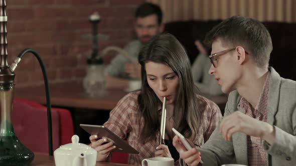 Couple Using Digital Tablet and Smoking Hookah in Shisha Cafe alt
