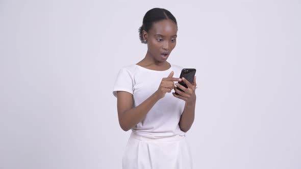 Young African Woman Looking Shocked and Stunned While Using Phone alt
