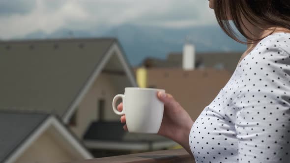 Close Up Young Woman Drinking From a White Cup on the Balcony with Amazing View on the Mountains and alt
