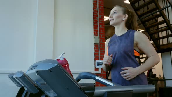 Attractive Young Sports Woman Running on Treadmill and Drinks a Water