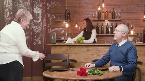 Senior Woman Arrives on a Date and Her Partner Gives Her Flowers alt
