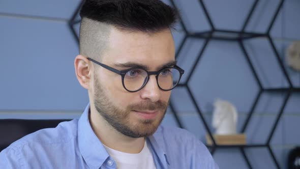 Close-up portrait of handsome man wearing glasses looking at laptop working in office