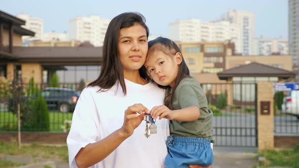 Cheerful Woman Shows Keys of Apartment Holding Daughter alt