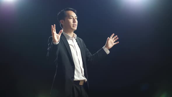 Side View Of Asian Speaker Man In Business Suit Holding His Hands Together While Speaking alt