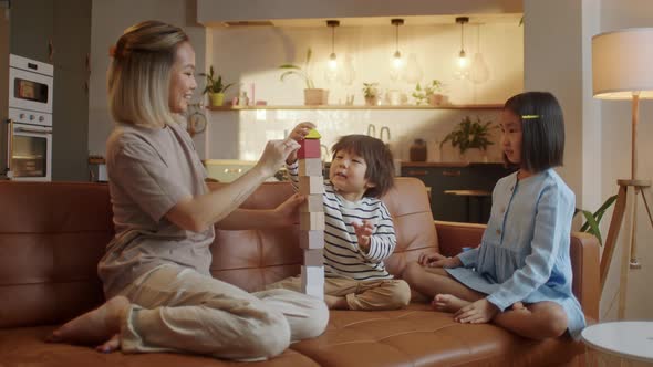 Happy Asian Young Mother and Two Little Children Sitting at Sofa and Playing Together alt
