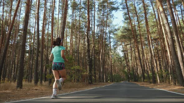 Athletic Girl Runs Along the Road in a Pine Forest alt