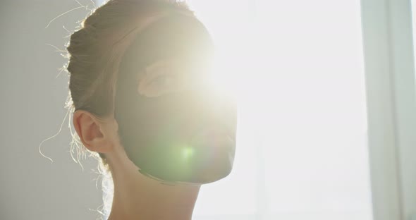 a Young Woman in a Cosmetic Mask Against the Background of the Sun is at Home alt