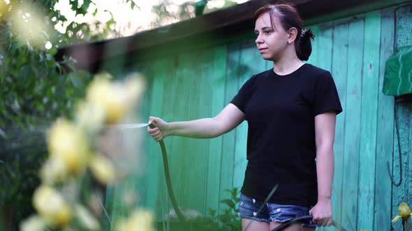 Young Woman Watering Vegetable Garden From Hose. Close Up of Female Watering. Concept of Summer and alt