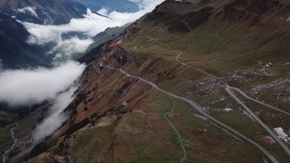 Clouds hang in the valley of rocky mountain landscape criss-crossed by winding roads alt