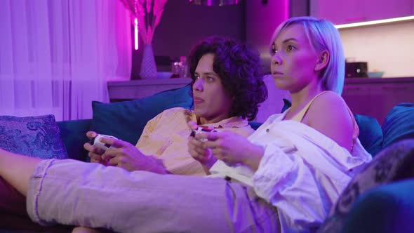 Happy Young Couple Playing a Video Game Sitting at Home on a Sofa During Self Isolation on alt